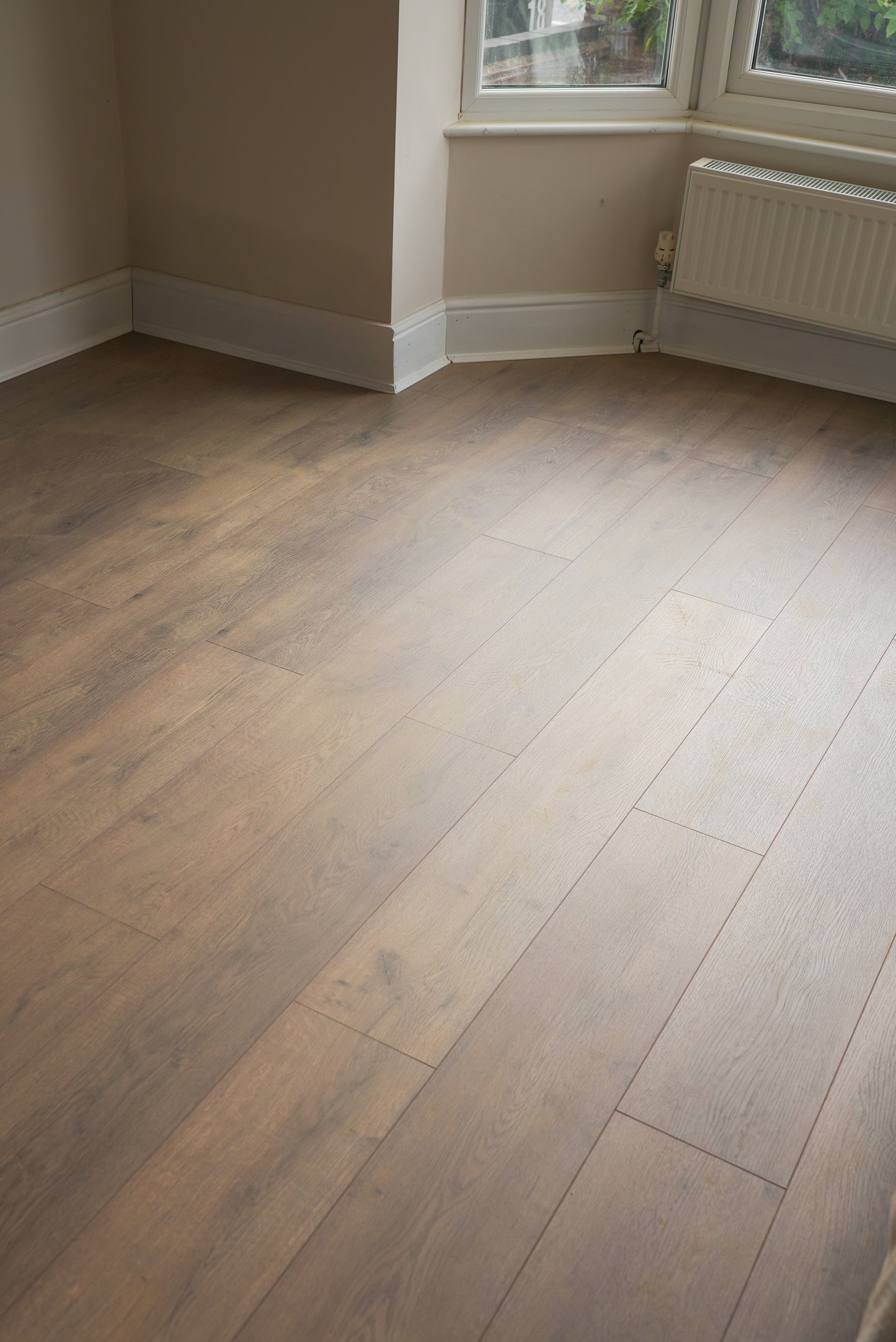 Wooden floor in a room with a window and radiator.