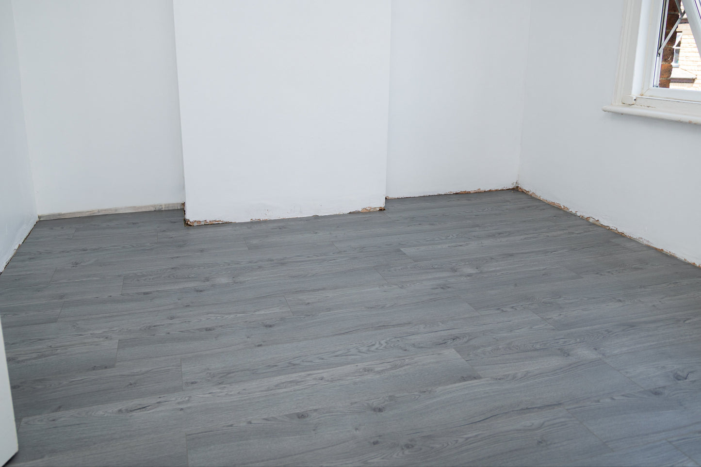 Empty room with gray wooden flooring and white walls.