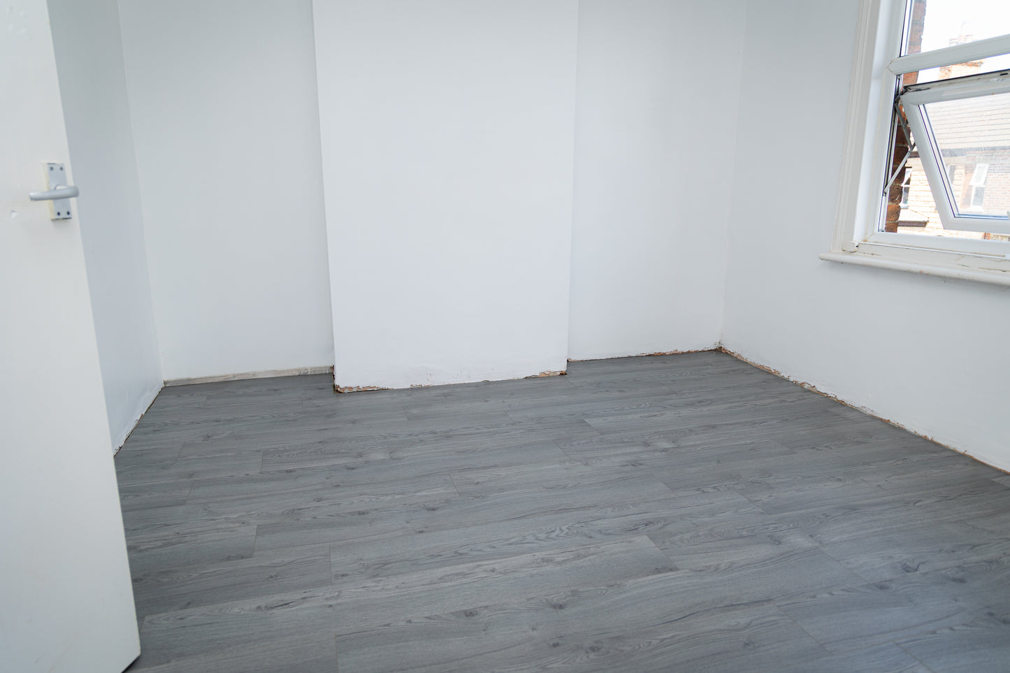 Empty room with gray wooden flooring and white walls.