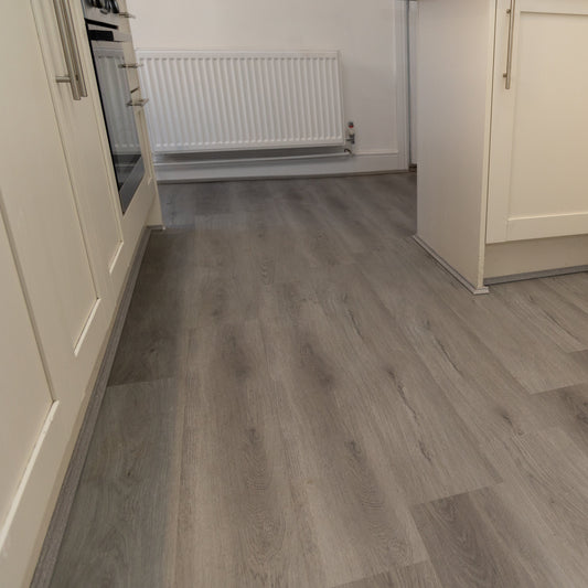 Gray wood-look laminate flooring installed in a modern kitchen with cream-colored cabinets and silver handles.