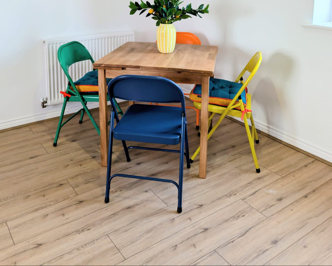 Dining area with a wooden table and colorful chairs on a wooden floor.