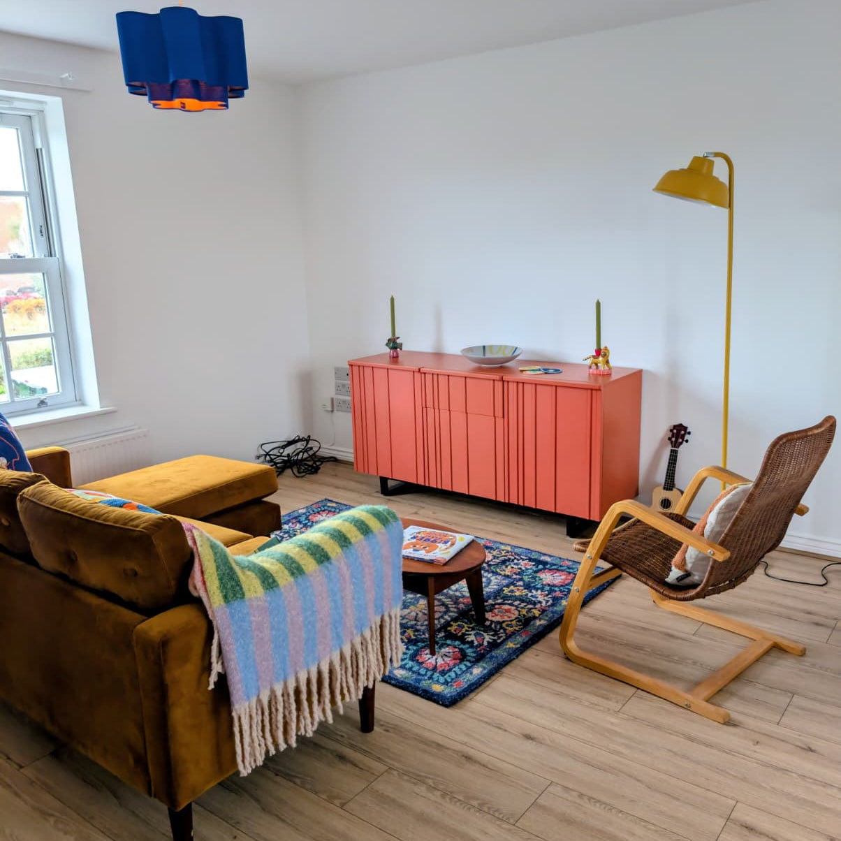 Living room with brown sofa, pink cabinet, and colorful rug.